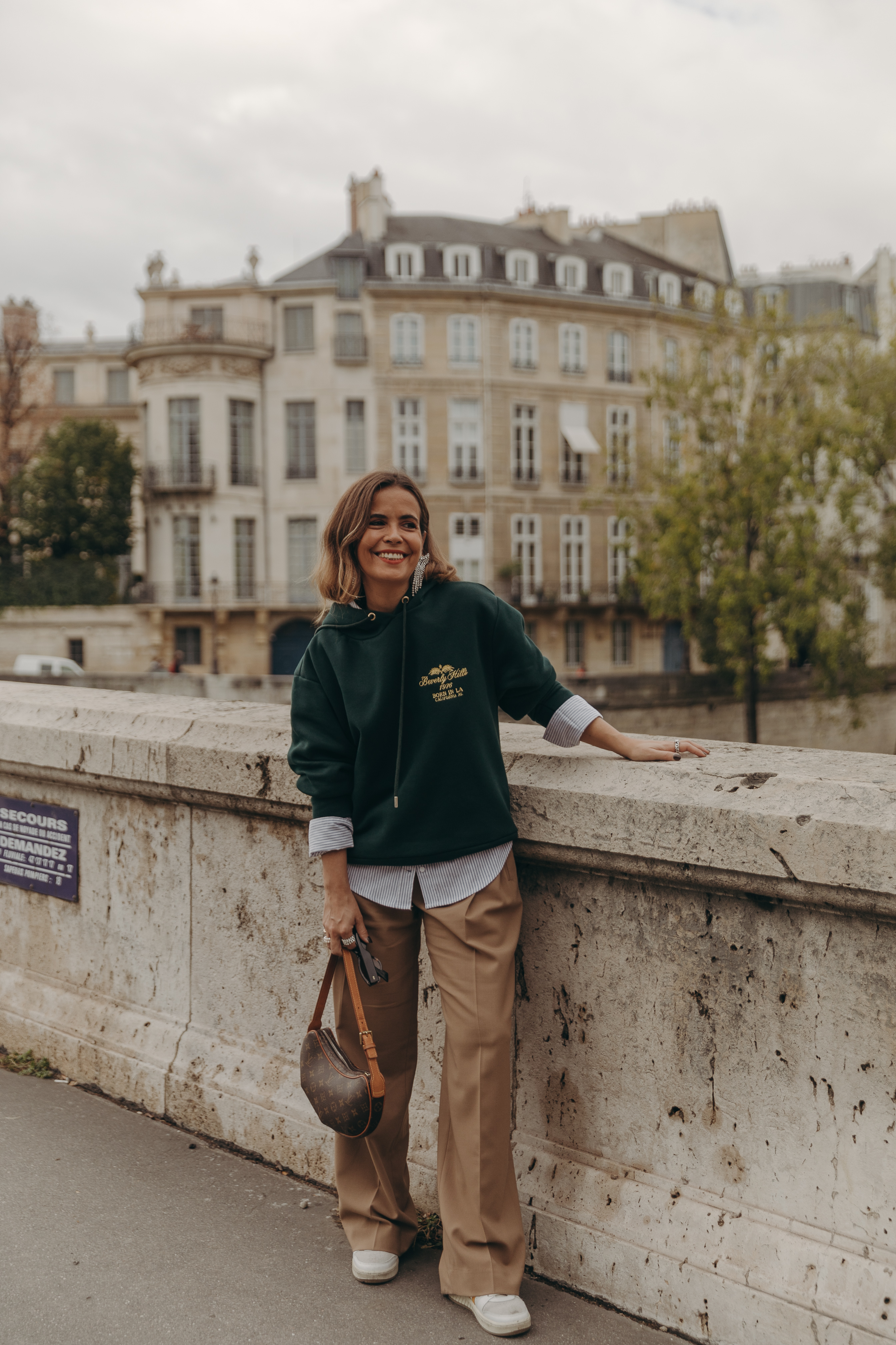 Sara from Collage Vintage at Paris Fashion Week wearing a oversize green sweatshirt, camel trousers, Louis Vuitton vintage bag and sneakers.