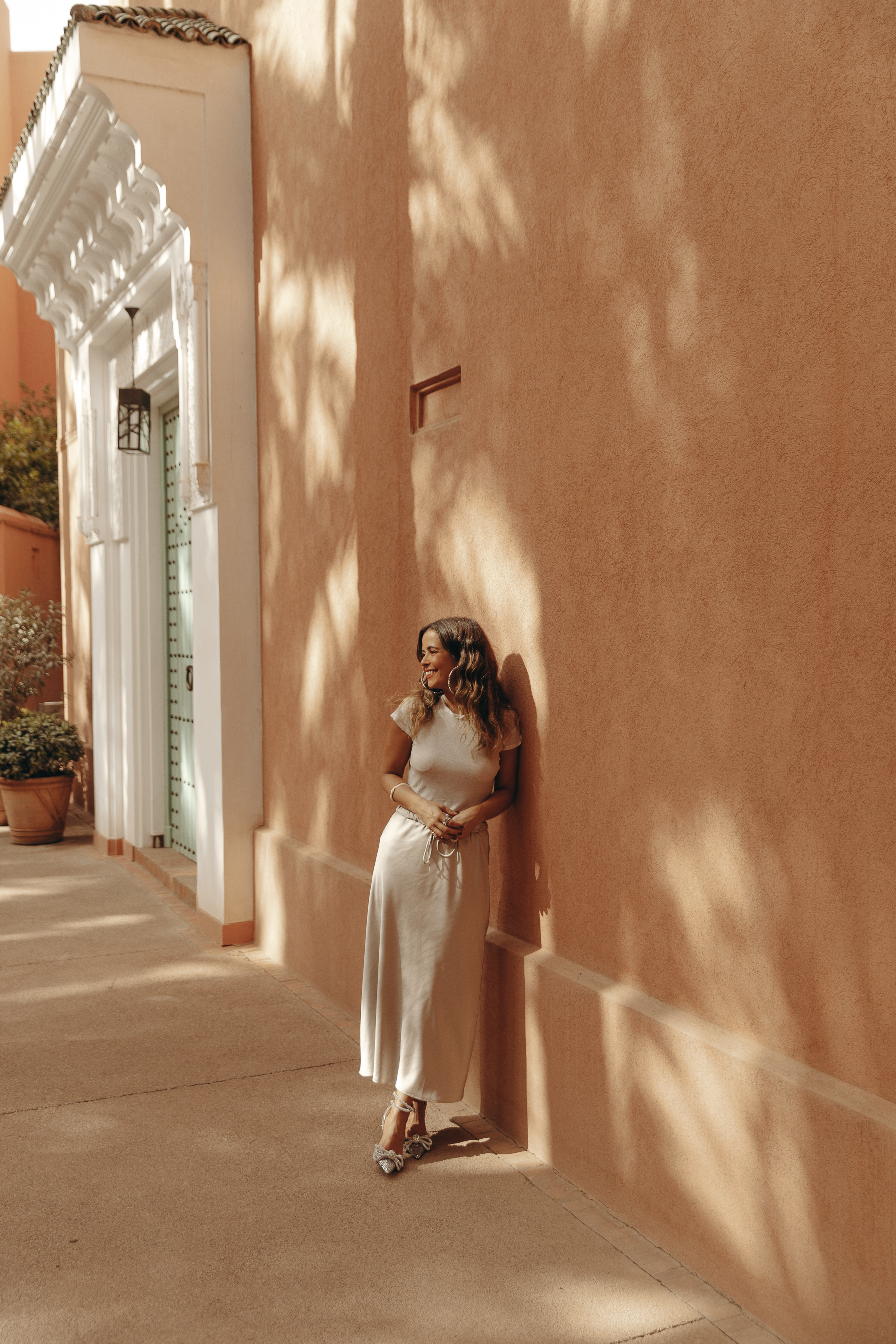 Sara from Collage Vintage wearing a satin long skirt, Mach & Mach crystal embellished pumps and maxi hoops in a palm tree garden in Marrakech